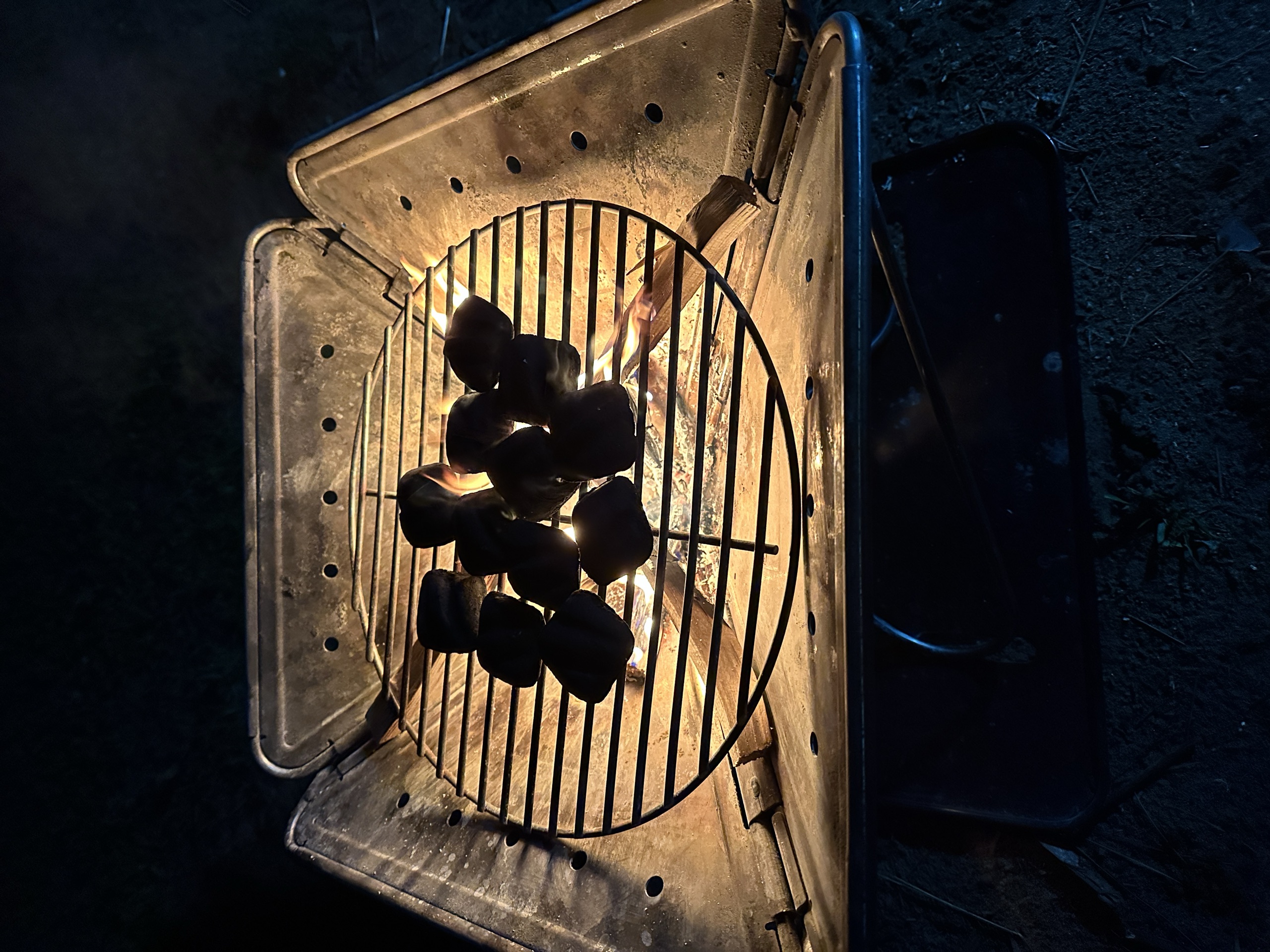 Black charcoal pieces glowing orange in a small portable grill at night